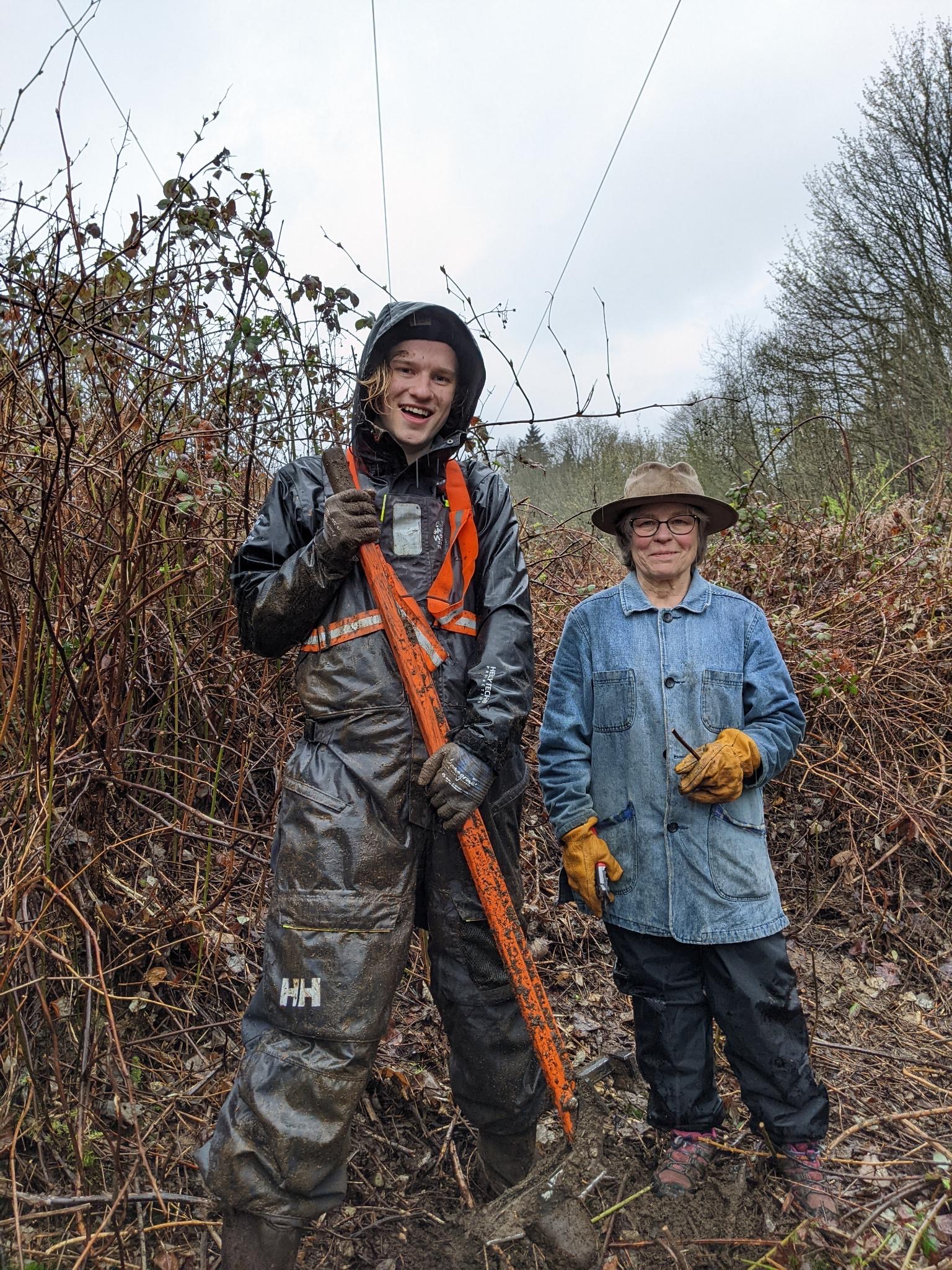 A muddy Matthew and a volunteer pose at the Rubus Restoration worksite removing blackberry