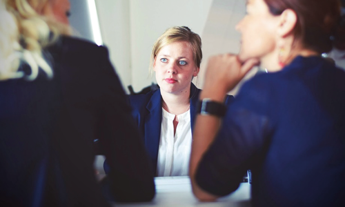 Woman in business attire sitting with other peers, being ignored. 