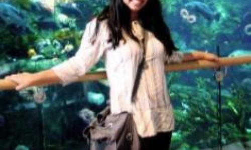 Mubnii smiling with her hands in an open position, in front of an aquarium