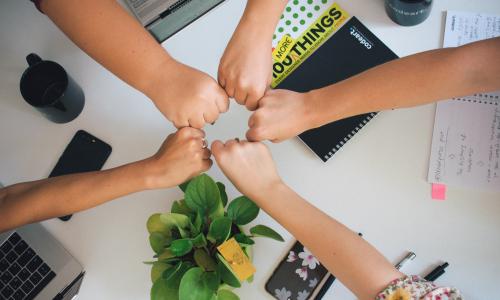 Five people fist bumping over an office desk