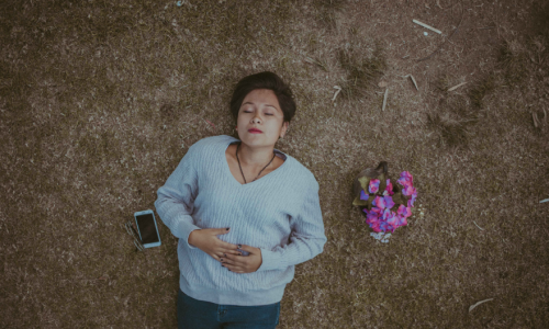 A woman lying on her back in a field with roses and a phone next to her.