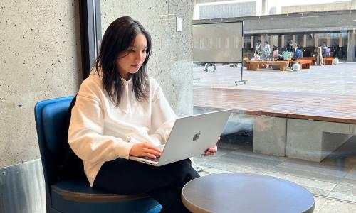 Student sitting in SFU library by window working on laptop