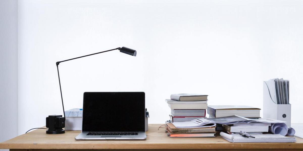 From left to right a lamp, laptop, and a stack of books are next to each other on desk