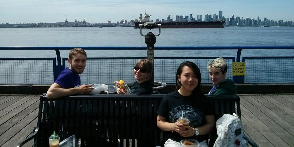 Lea sitting on a bench on the docks having lunch with three other people