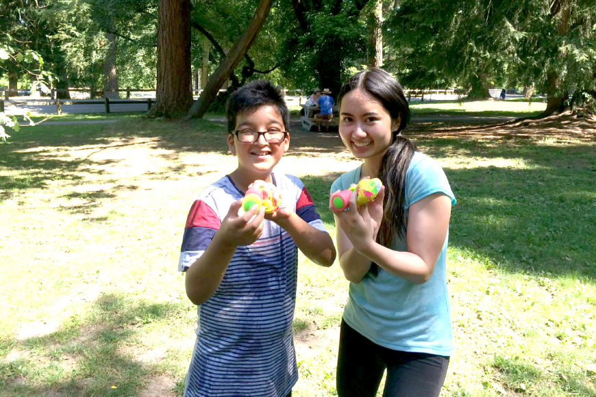 Author and her young male student smiling at the camera and holding up tennis balls in both hands.The picture is set in a field with trees in the background.