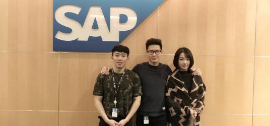 Three people posing in front of the SAP logo 