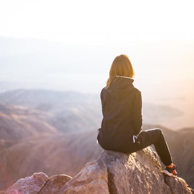 a girl sitting on top of a mountain staring into the sunset