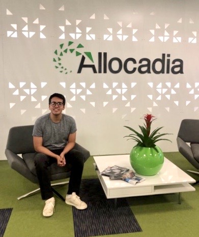 Image of the author sitting in the lounge in front of the company's logo 