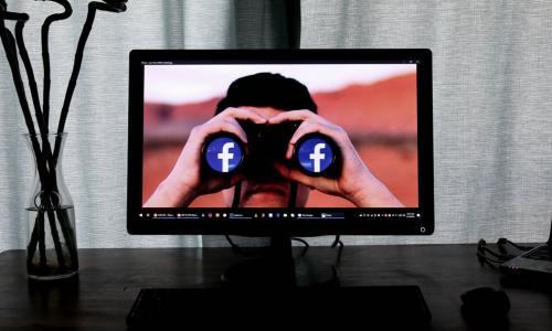 a computer screen showcasing a man holding binoculars with Facebook icons as the lens