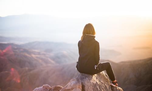 a girl sitting on top of a mountain staring into the sunset