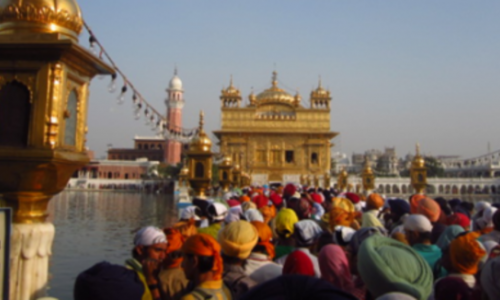 A large group of people walking towards the Golden Temple situated on a lake