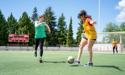 Two girls kicking around a soccer ball on a soccer field. 
