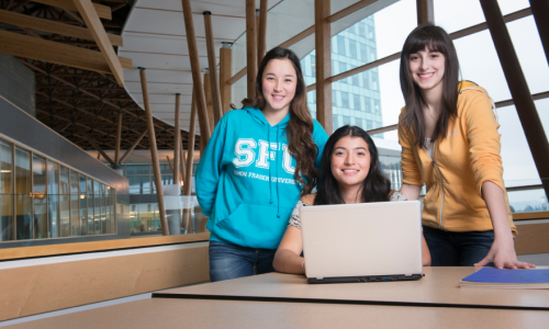 Three SFU students standing in front of a laptop.