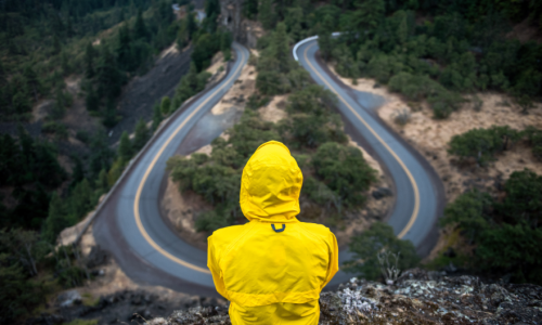Person wearing a raincoat sitting above an empty road 