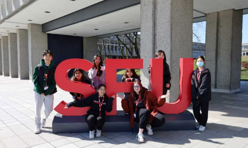 Co-op students standing outside around a sign that says "SFU"