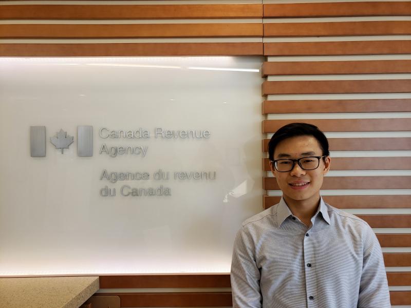 Matthew Lee standing in front of a board with the Canada Revenue Agency logo in English and french