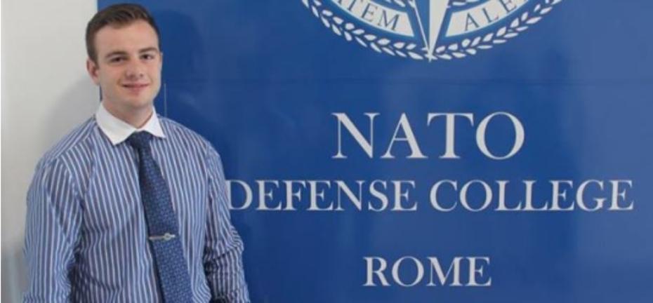 Cornel standing in front of a NATO Banner