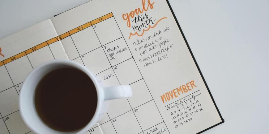 A cup of coffee placed on a written planner with the word "goals" next to it