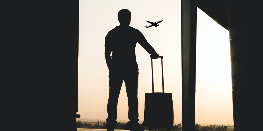 silhouette of person standing with suitcase, watching an airplane takeoff