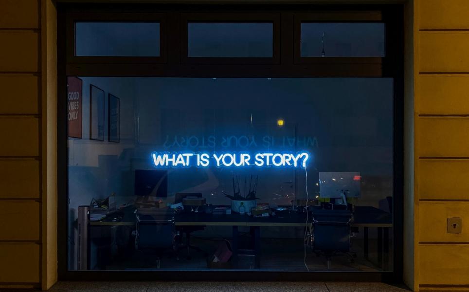 Neon lights on a window reading "What is your story?"