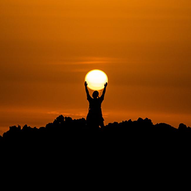 Person standing in the sunset holding up the sun. 