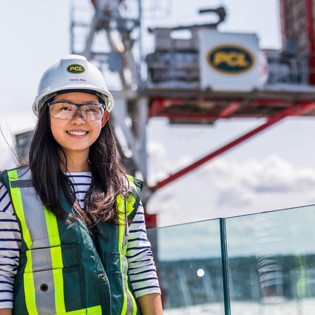 girl with safety hat, vest, and glasses standing in front of construction site