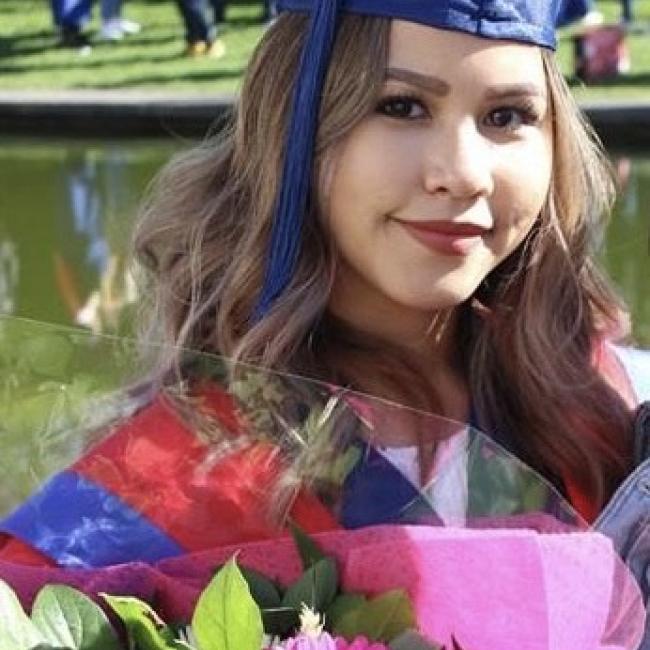 Image of Nikki in convocation cap and gown holding flowers at her Ugrad Communication Convocation
