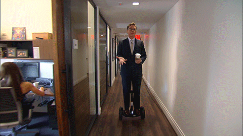 Stephen Colbert hoverboarding down a hallway while being tossed a burrito