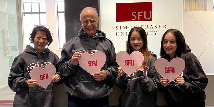 (Left to Right): Claudia, Laurie, Kimberly, and Kiara holding heart shaped SFU signs