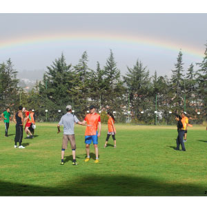 group of people playing ultimate frisbee, rainbow in the background