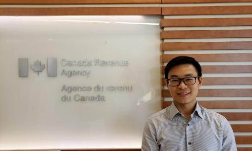 Matthew Lee standing in front of a board with the Canada Revenue Agency logo in English and french