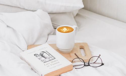 a bed spread containing coffee mug, glasses, and a book