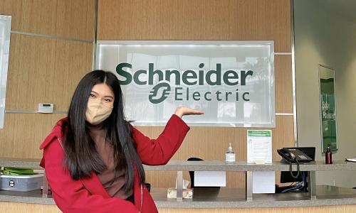 Girl standing next to sign that says "Schneider Electric", pointing at sign.