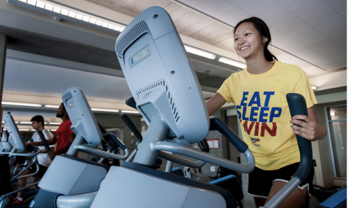 A person running on a treadmill wearing a yellow shirt. 
