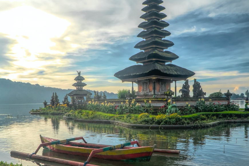Indonesian pagoda surrounded by a lake and a boat floating in front