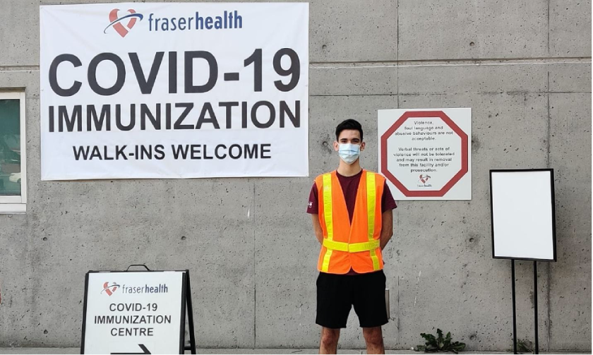 A picture of Alan in front of a Fraser Health COVID-19 VACCINATION poster.