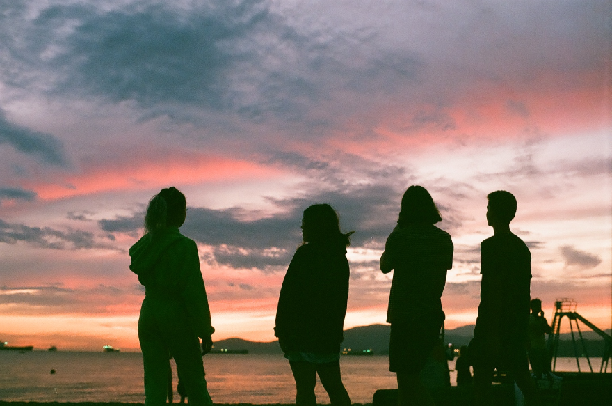 Four silhouettes on a beach with a sunset behind them. 