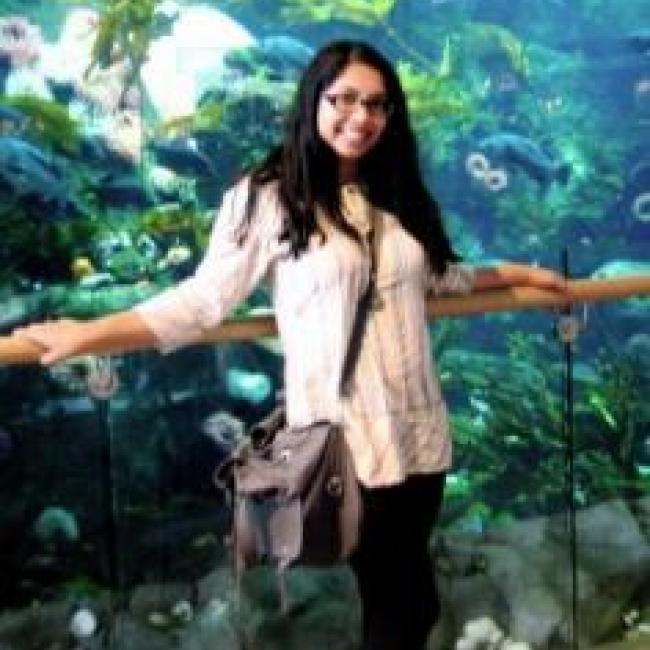 Mubnii smiling with her hands in an open position, in front of an aquarium