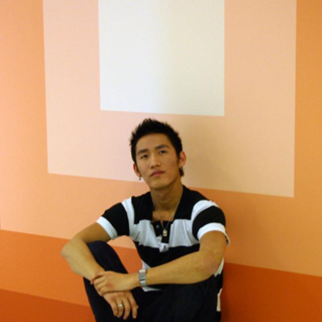 A person sitting down while thinking in front of an orange wall.