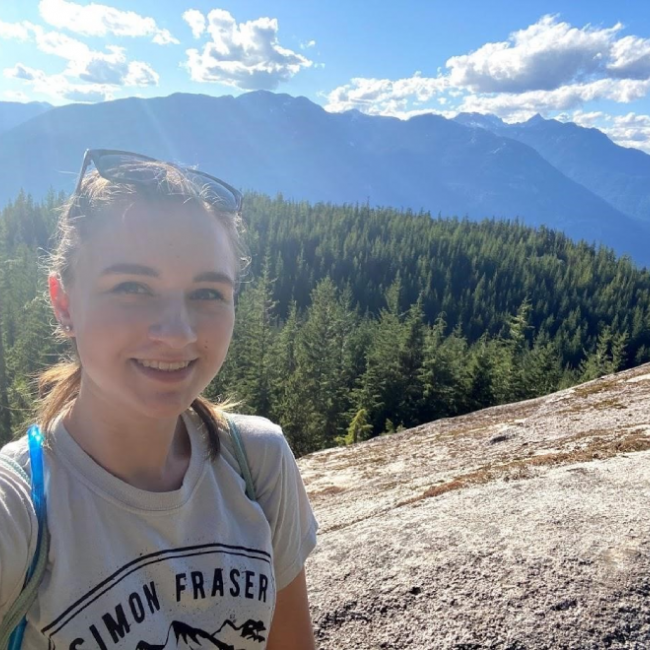 A picture of a woman talking a selfie in front of a mountain range