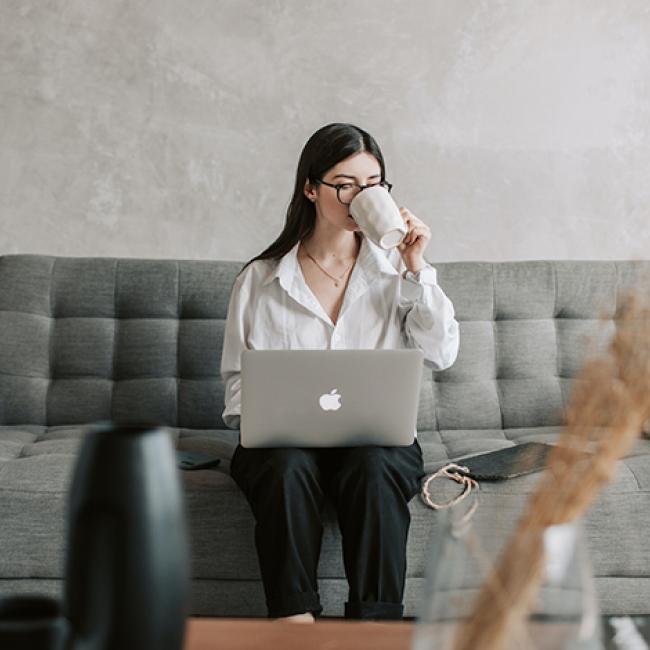 Woman sitting on a couch and drinking coffee while working on laptop