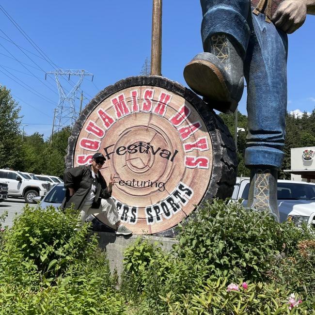 An image of Chloe Evangelista standing in front of a sign that says Squamish Days Festival, to commemorate a site visit to two Squamish Nation-owned businesses in Squamish, BC.