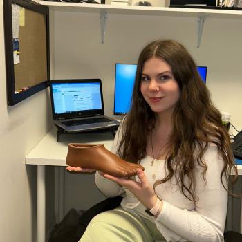 Brianna Larsen sits in an office setting displaying a prosthetic foot.