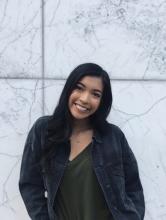 Marielle standing in front of a brick wall, smiling at camera with head tilted to the side