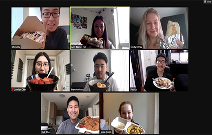 Seven coworkers are on a zoom call and are holding up their lunches to their cameras.