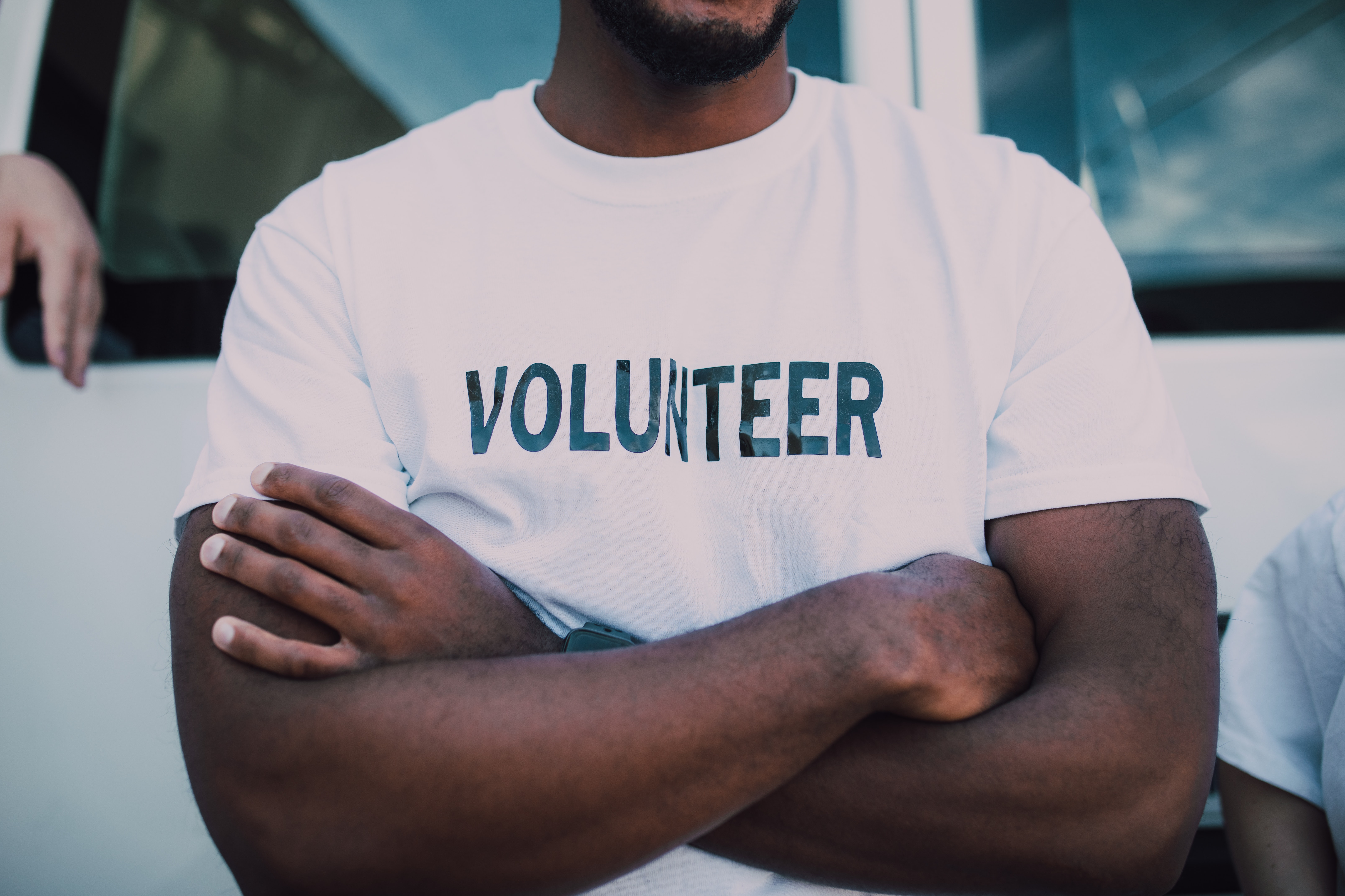 Person with arms crossed wearing a white shirt that says volunteer.