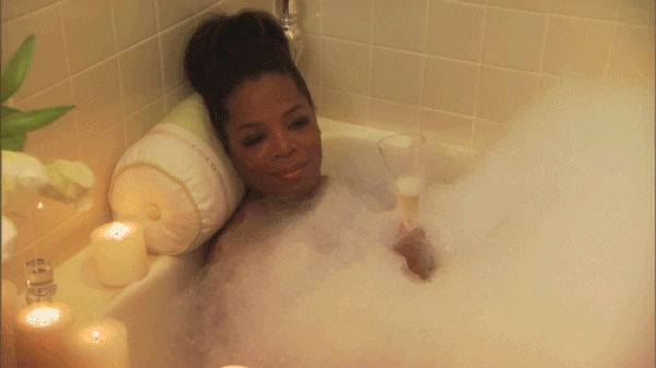 Gif of Oprah Winfrey taking a bubble bath in candle light with a glass of champagne in her hand