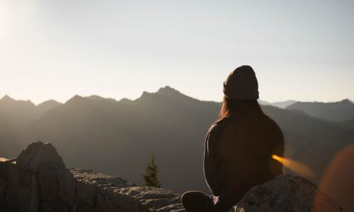 the back of a woman on top of a mountain peak taking in the view