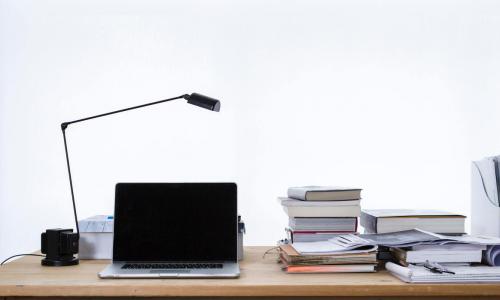 From left to right a lamp, laptop, and a stack of books are next to each other on desk