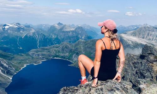 Woman sitting on cliff, looking out at view of mountains and body of water